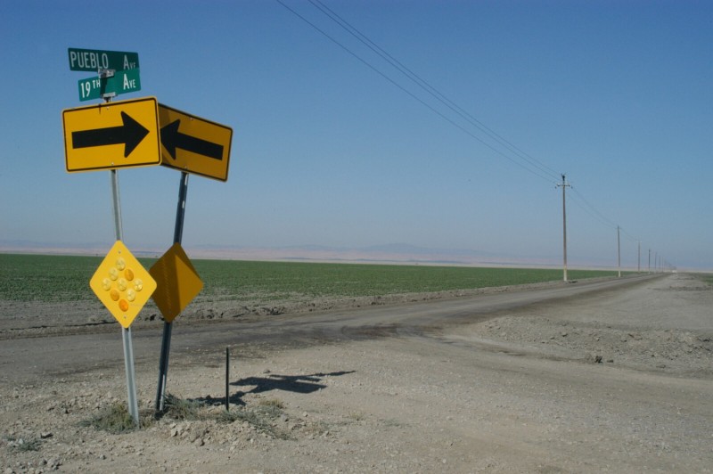 Desolate road with two yellow arrow signs pointing at one another.